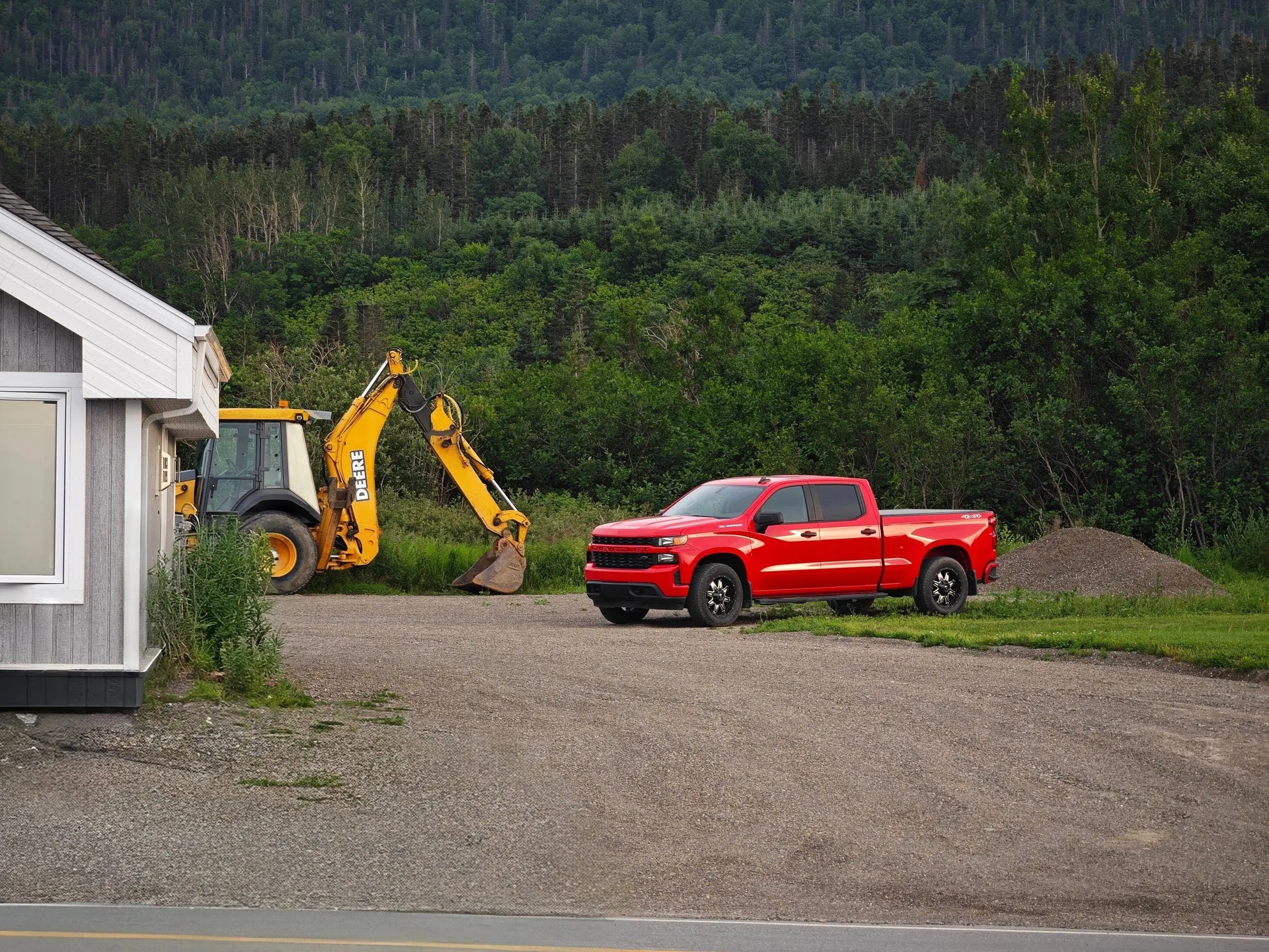 Contractor's red pickup and backhoe in a rural driveway
