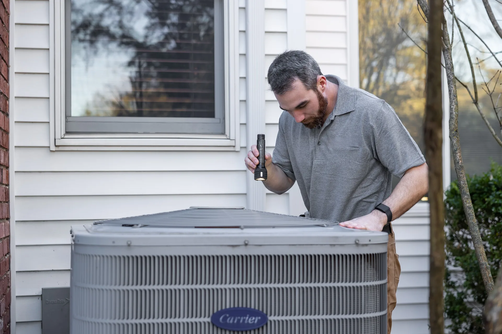HVAC technician servicing an outdoor unit beside a house
