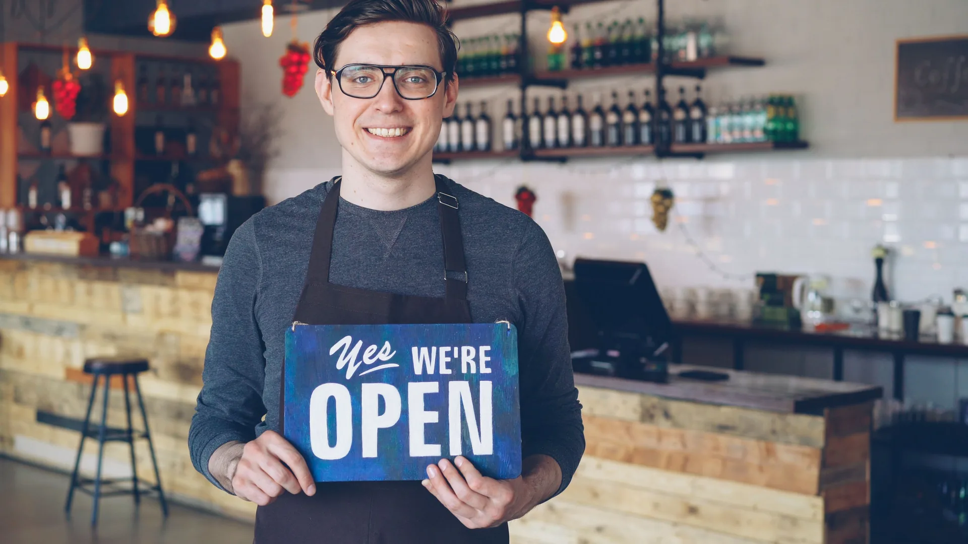 Coffee shop owner holding an open sign behind the counter